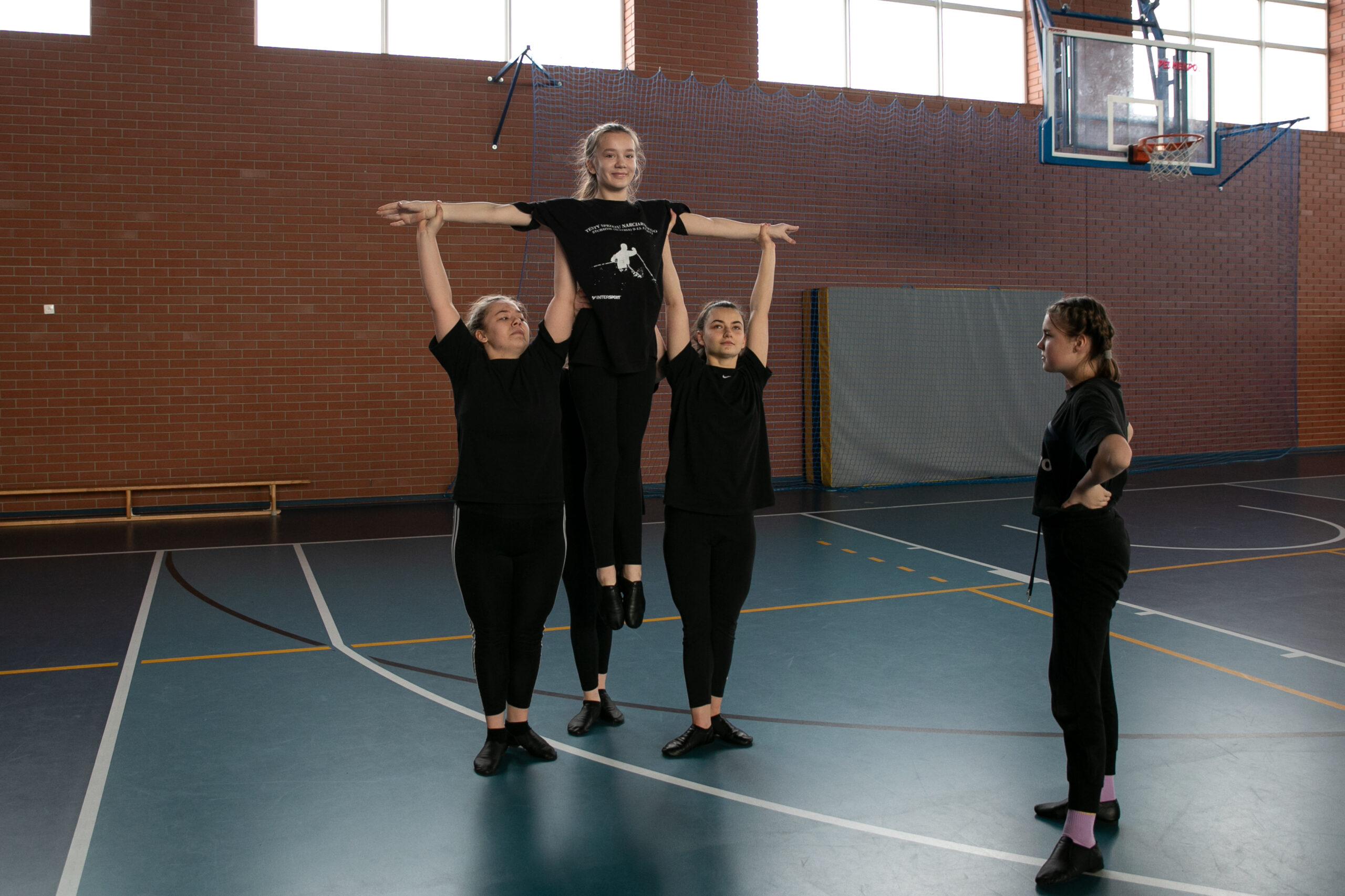 pięć dziewczyn w czarnych ubraniach wykonujące podnoszenie taneczne na hali gimnastycznej