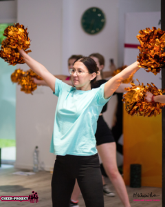 Kurs trenerski BASIC, cheerleaderka trzymająca pompony w pozycji high V